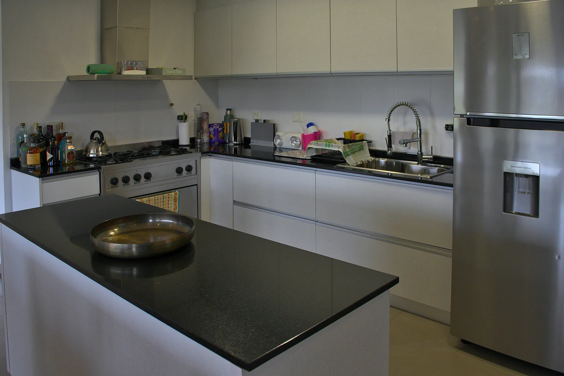 Cocina blanca con isla y mesada de granito negro.